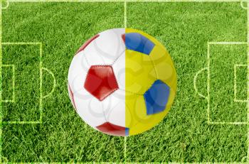 Soccer ball colored by flag of Poland and Ukraine at green grass