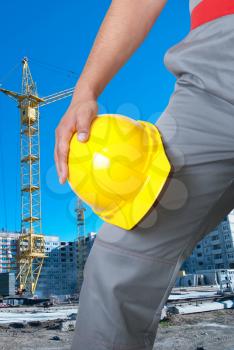 Closeup  of yellow helmet at builder hands on building background