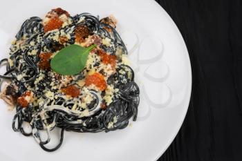 Black pasta with cuttlefish ink, parmesan cheese basil and red caviar. The concept of Italian cuisine.