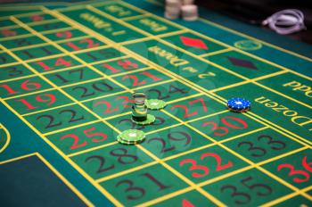 Casino, gambling and entertainment concept - green roulette table with colored chips ready to play