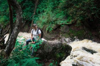 Man traveler with backpack sitting on rock in the forest. Travel lifestyle or adventure vacations concept