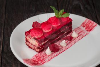 Plate with piece of delicious red velvet cake on dark wooden background