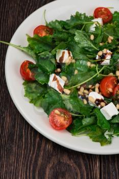 Green salad with vegetables: greens, arugula, tomato, cheese, pine nuts and sauce on dark wooden background