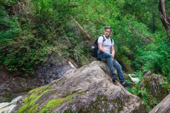 Man traveler with backpack sitting on rock in the forest. Travel lifestyle or adventure vacations concept