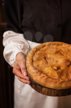 Pie from potato meat cheese and vegetables. Freshly baked pie in hands of woman in uniform