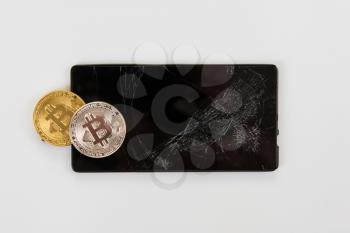 Bitcoin coin on broken phone on white