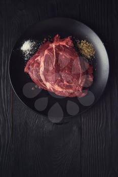 Fresh raw beef meat steaks in the black plate with spices on black wooden background