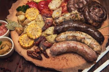 Grilled different meat and fish sausages with vegetables and spices on wooden background