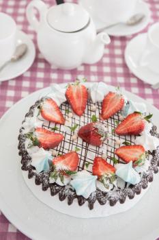 Tasty strawberry cream cake on checkered table, with tea set