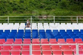 Lonely woman with protective mask on the empty stadium outdoor. Empty tribune due to pandemic Covid-19. Concept of pandemic life , empty stadiums, distance from viewers, safety.