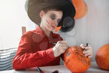 Halloween carnival or masquerade concept. Happy teen boy in costume drawing a pumpkin for the Halloween celebration.