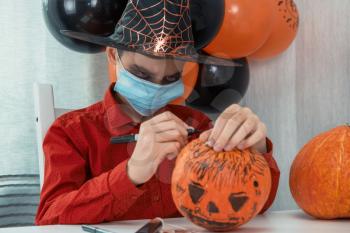 Teen boy in costume and face masks to protect against COVID-19 drawing a pumpkin for the Halloween celebration. Halloween carnival with new reality with pandemic concept.