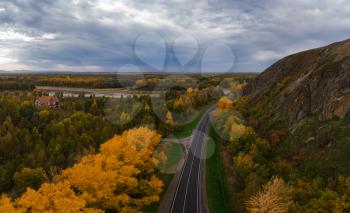 Aerial view of road in beautiful autumn Altai forest. Beautiful landscape with empty rural road, golden autumn in altai: trees with red, yellow and orange leaves.