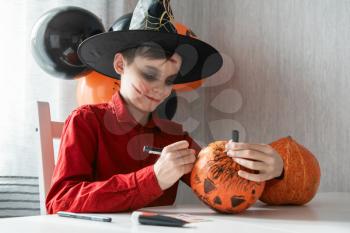 Teen boy in costume drawing coronavirus image on the pumpkin for the Halloween celebration. Halloween carnival with new reality with pandemic concept.