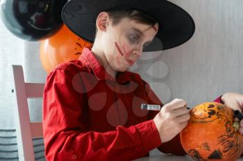 Teen boy in costume drawing coronavirus image on the pumpkin for the Halloween celebration. Halloween carnival with new reality with pandemic concept.
