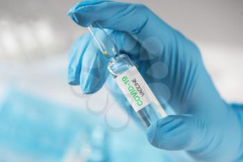 Coronavirus vaccine concept: covid-19 vaccine in hand with blue protective gloves.