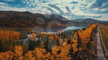 Aerial view of road and lake in beautiful autumn Altai forest. Beautiful landscape with empty rural road, golden autumn in altai: trees with red, yellow and orange leaves.