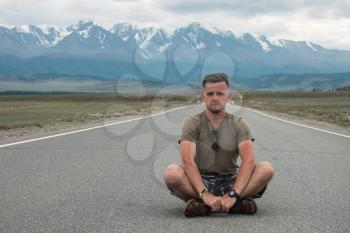 Handsome young caucasian man sitting on road in Altai mountain.