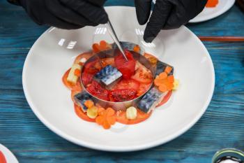 Process of cooking escabeche fish dish with caviar: mackerel in marinade with vegetable, on a plate on the wooden blue background.