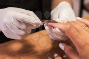 Closeup photo of a woman in a nail salon receiving a manicure by a beautician with nail file.