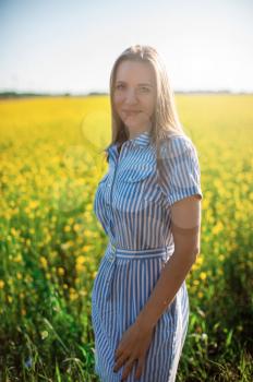 Beautiful woman in field with yellow flowers at summer sunset