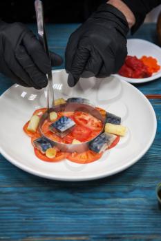 Process of cooking escabeche fish dish with caviar: mackerel in marinade with vegetable, on a plate on the wooden blue background.