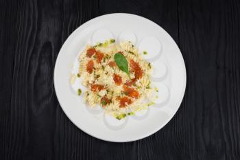 Pasta with parmesan cheese basil and red caviar on black wooden background