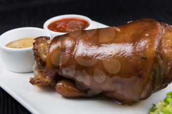 Tasty pork knuckle with sauces and vegetables on a white background