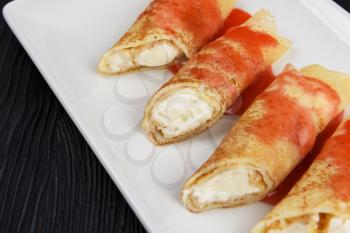 Pancakes or russian blini stuffed with cream sauce on a white plate.