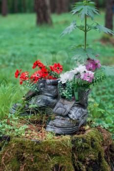 Touristic boot with flowers in the forest. Summer background with forgotten boots and wild flowers. Concept of summer season and traveling.