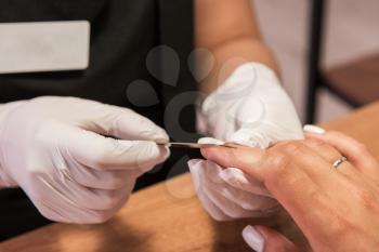 Closeup photo of a woman in a nail salon receiving a manicure by a beautician with nail file.