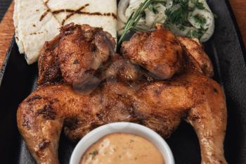 Appetizing grilled juicy chicken with golden brown crust served with barbeque sauce, rosemary and pita bread.