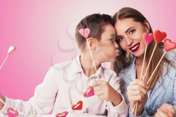 Happy Valentines Day or Mother day. Young boy spend time with his mum and celebrate with gingerbread heart cookies on a stick on a pink background