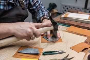 Man working with leather textile at a workshop. Concept of handmade craft production of leather goods. Foreground focus