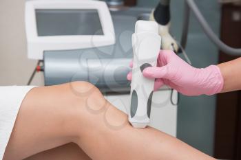 Specialist makes skin tone measurements on a womans leg, to determine the settings for hair laser depilation. First step before depilation. Cosmetology and SPA concept