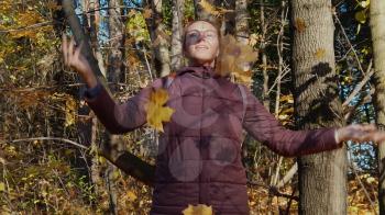 Beautiful woman throws up leaves in the autumn forest and enjoys good weather. Slow motion video