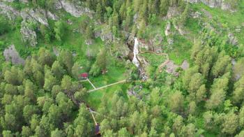 Drone flying over a green forest with waterfall in the Altai mountains. Aerial Drone footage 4K. Beautiful nature summer landscape.