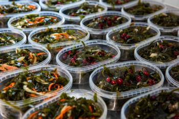Different fish and chuka wakame laminaria seaweed salad in plastic bowles. Concept of healthy food production or delivery food