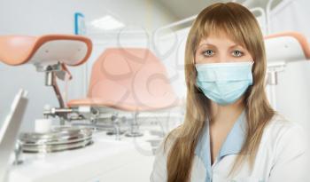 Female gynecologist in protective mask and whitecoat with gynecological vaginal retractor in hand