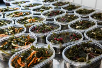 Different fish and chuka wakame laminaria seaweed salad in plastic bowles. Concept of healthy food production or delivery food