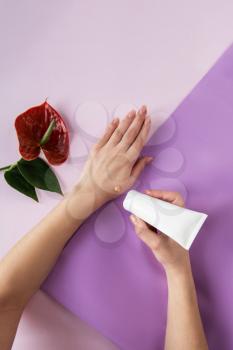 Young woman applying hand cream at color purple background