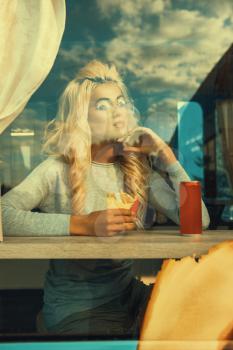Fast street food concept - beauty young blonde woman eating a burger and soda water into the food truck