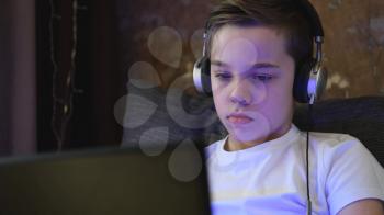 Handsome teen or young boy at home with laptop and headphones. Concept of home remote learning or school homework
