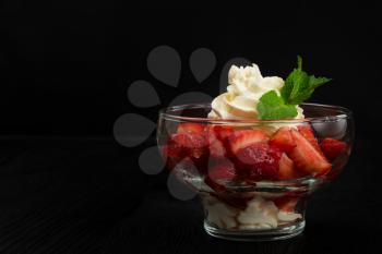 Strawberry with cream decorated with mint leaf on black wooden background, with copyspace, food and drink concept