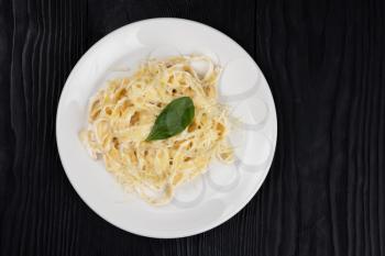 Pasta with sauce and basil in plate on black wooden background