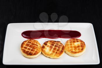 Cottage cheese pancakes on a dark background. Syrniki with berries jam on a white plate, food and drink concept