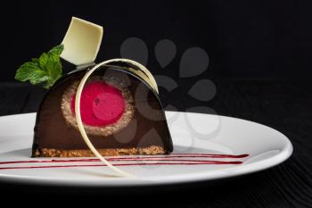 Delicious biscuit chocolate cake closeup with pink souffle decorated with mint and white chocolate on dark background