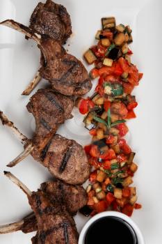 Roasted lamb ribs with vegetables on white plate on black wooden background