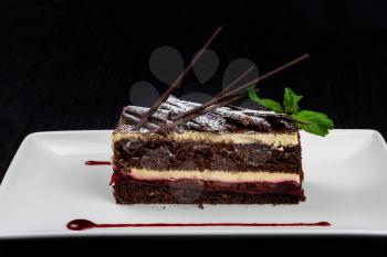 Plate with piece of delicious chocolate cake decorated with mint leaves on black background