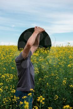 Man standing in yellow flowers field and holding circle mirror. Creative travel concept